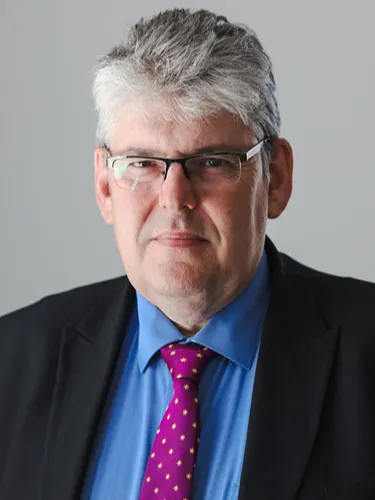 Paul Monks Paul Monks looking at the camera wearing a blue shirt, pink tie and black coat.