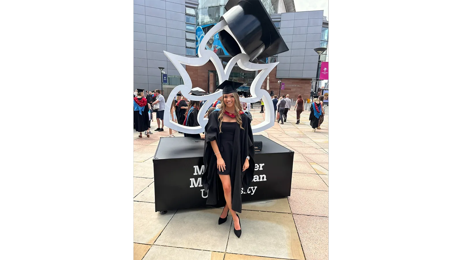 Georgia Wignall in a graduation gown and cap standing in front of a sign