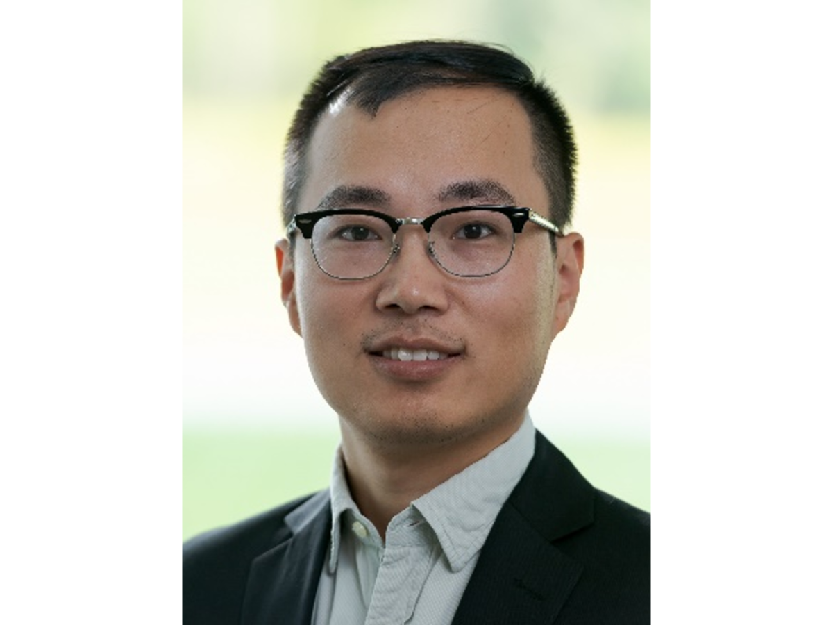 Guiliang Xu wearing glasses and a suit smiling to camera