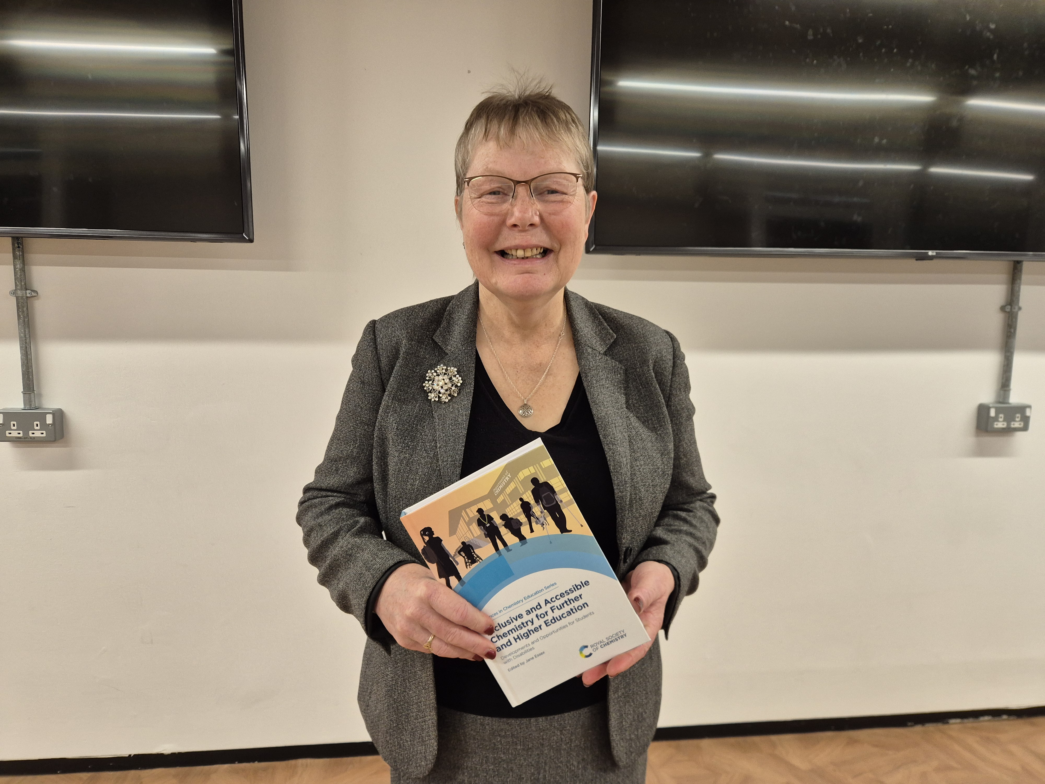 Dr Jane Essex smiles at the camera while holding a copy of the book
