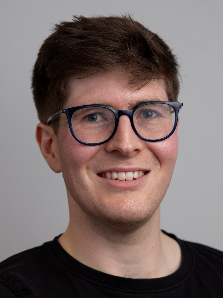 Hugh Ryan smiling to camera, wearing glasses, headshot