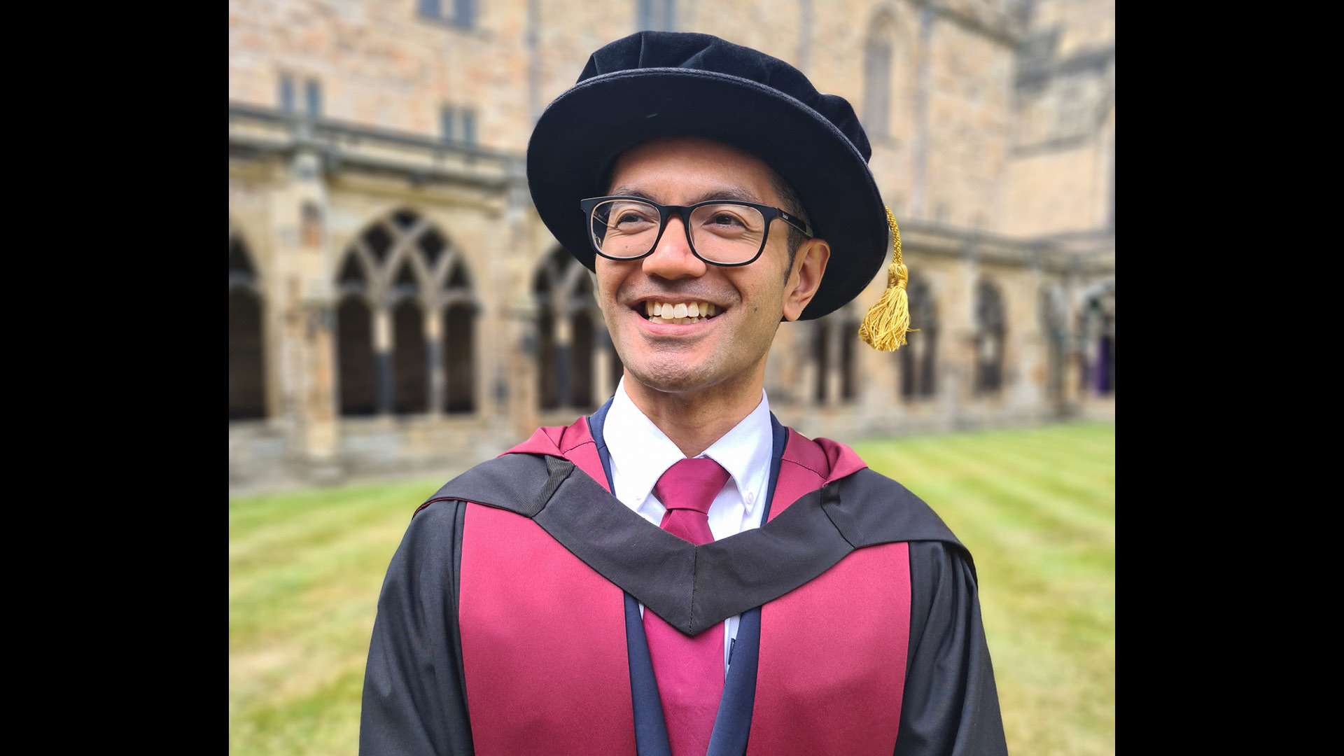 Benjamin Arenas in graduation attire smiling to camera wearing glasses