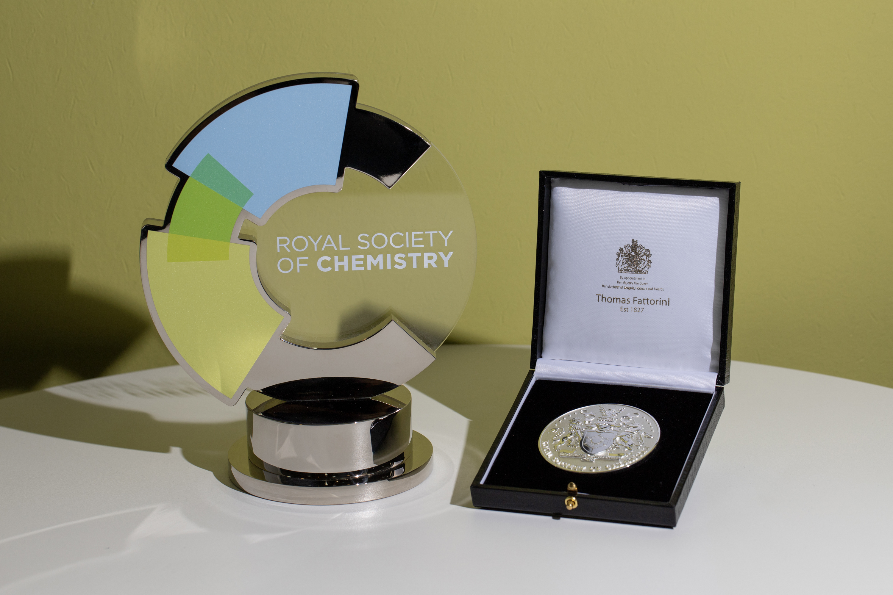 An RSC Prize trophy and medal sit on a white desk with a yellow background