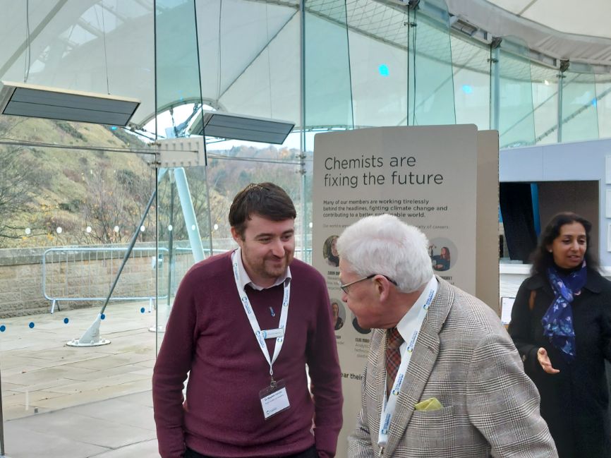 A member of our team speaks with one of the delegates at the Science and the Parliament event in front of a banner that reads "Chemists are fixing the future"
