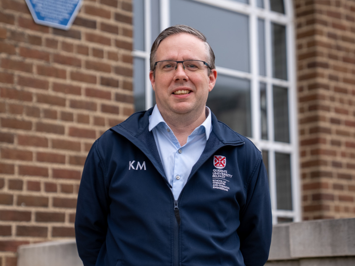 Kevin Morgan smiling to camera in glasses outside work building with a blue plaque on wall