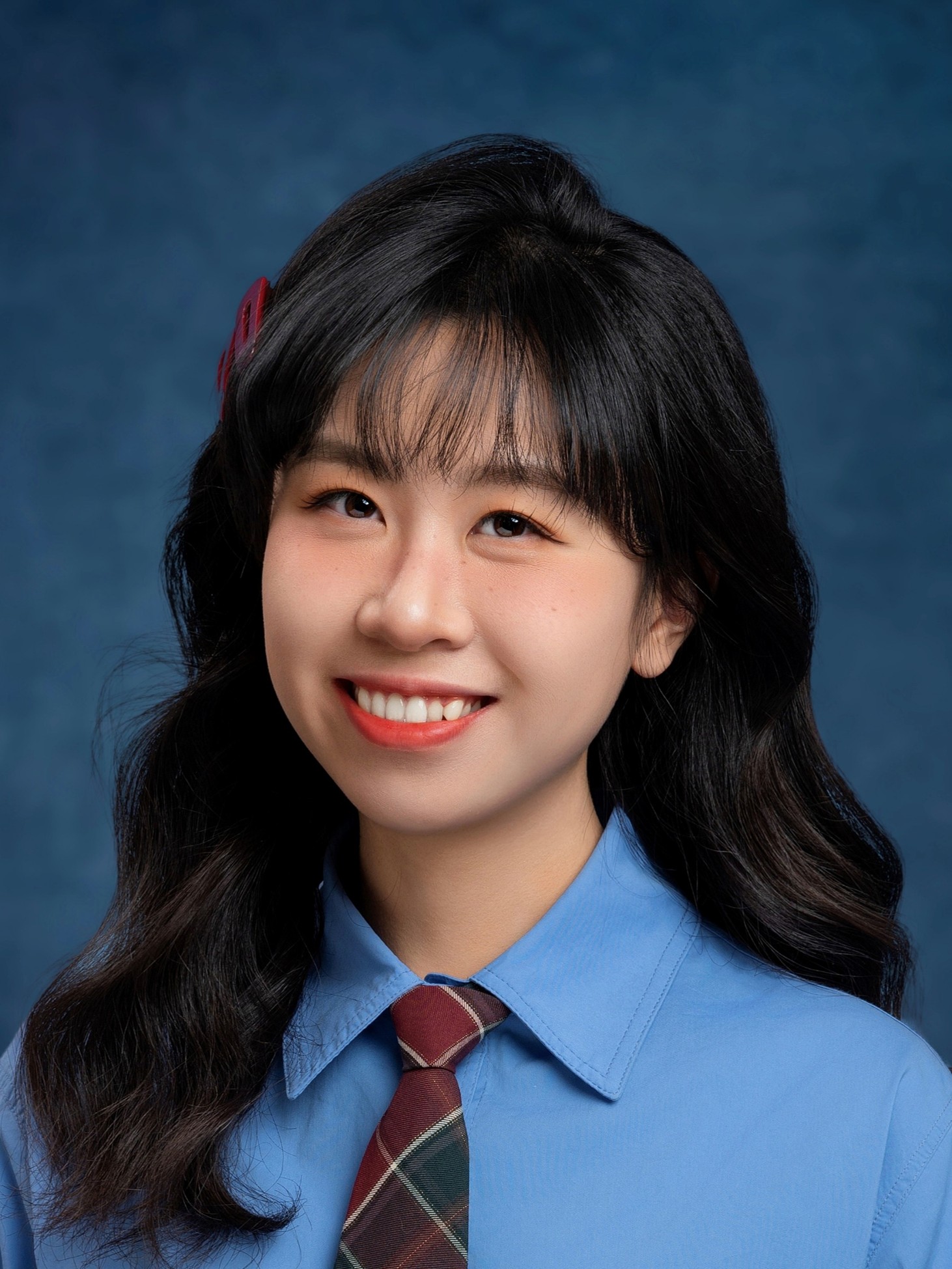 Xinyu Liu smiling, wearing a blue shirt and a plaid tie against a blue backdrop.