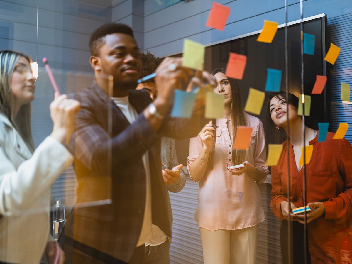 a group of people of mixed gender and race adding coloured Post-it notes on a glass wall