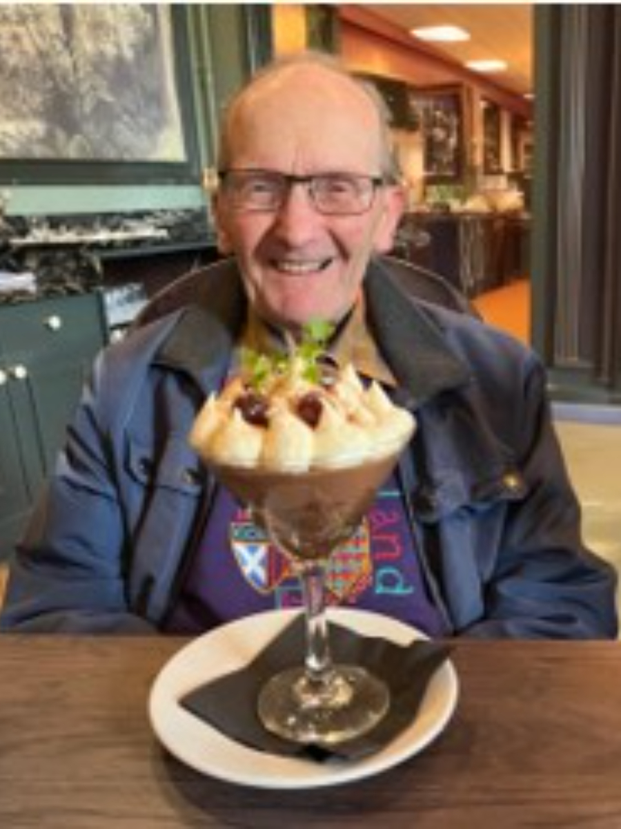 David Sammon smiling to camera with a big dessert in front of him in glass tall vase