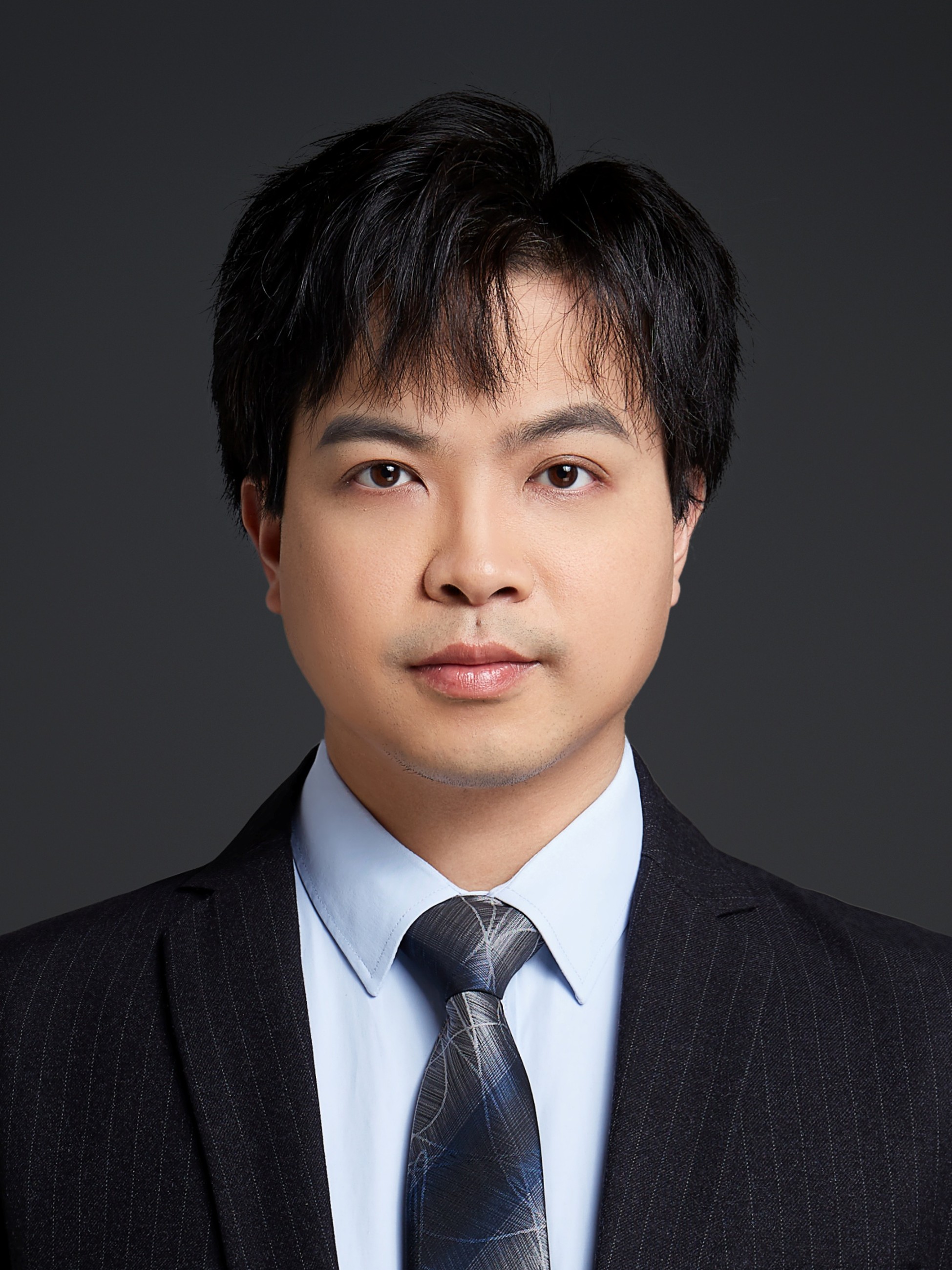 Headshot of Sen Xin, looking at the camera wearing a black blazer and tie