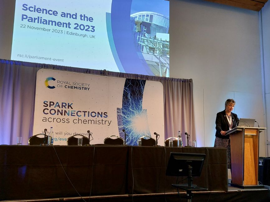 Professor Gill Reid, our president, addresses the crowd at Science and the Parliament 2023 while standing next to a pair of RSC backdrops
