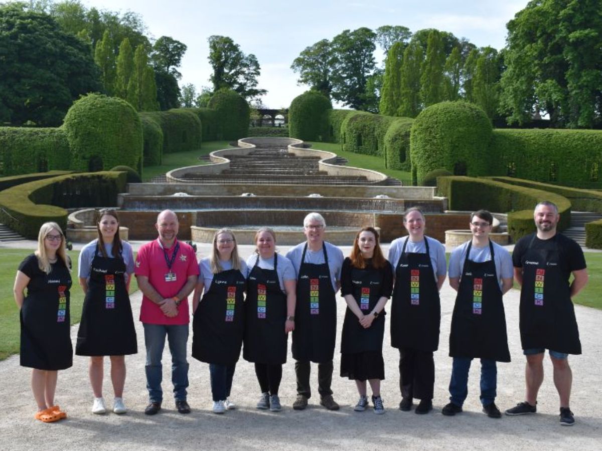 Ten volunteers in aprons in manicured gardens of alnwick