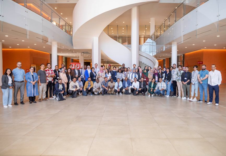 Around 50 or 60 participants of the GreenChemAfrica training school pose and smile in the reception area of a large, white, modern building